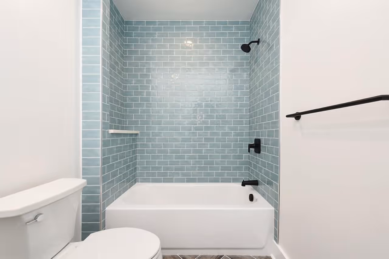 A remodeled bathroom with blue subway tile surrounding the tub