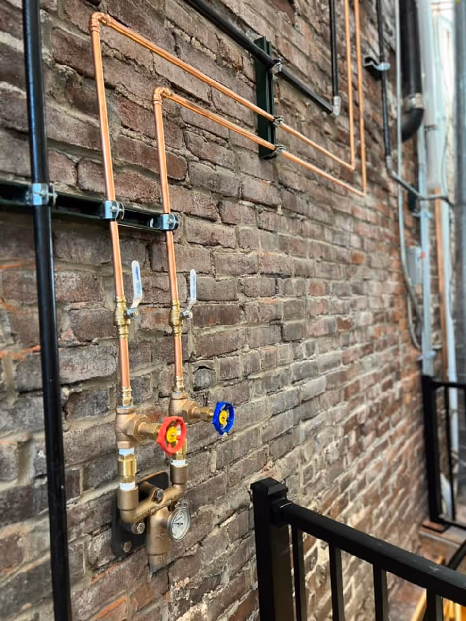 Copper supply lines and shutoff valves installed against an exposed brick wall